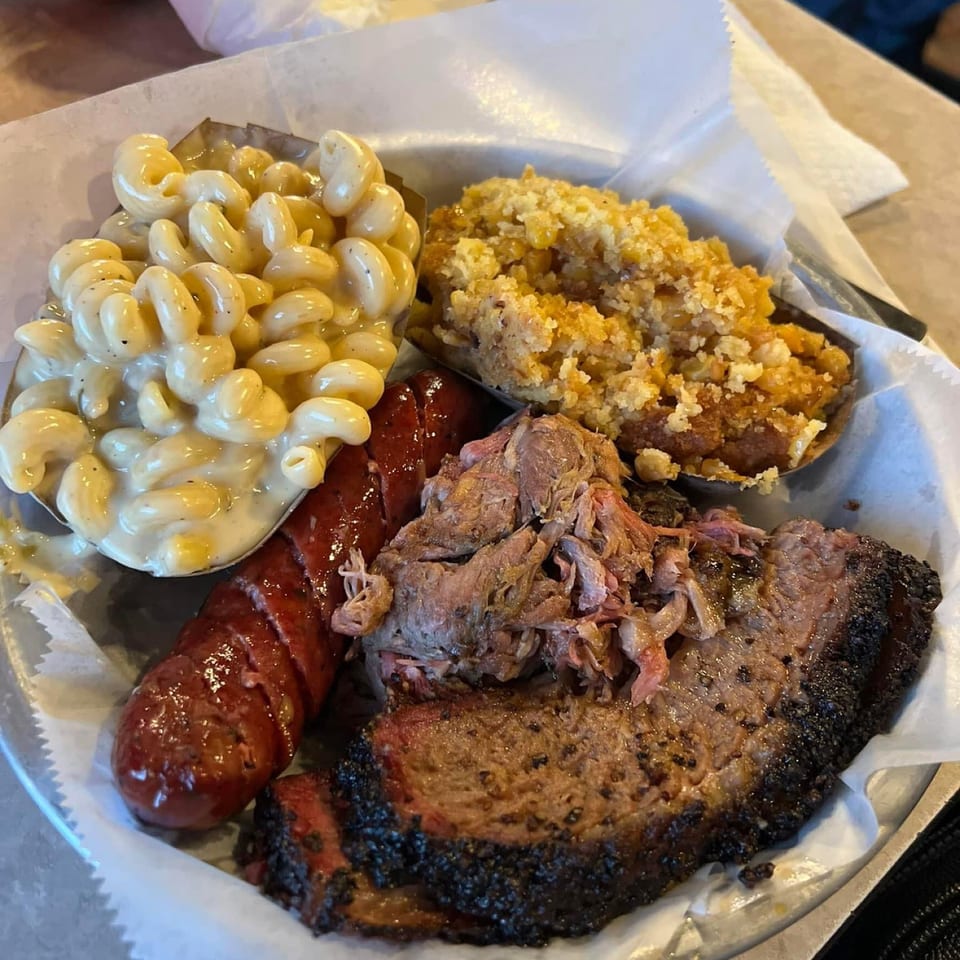 A BBQ platter with brisket, sausage, mac and cheese, and a corn casserole.
