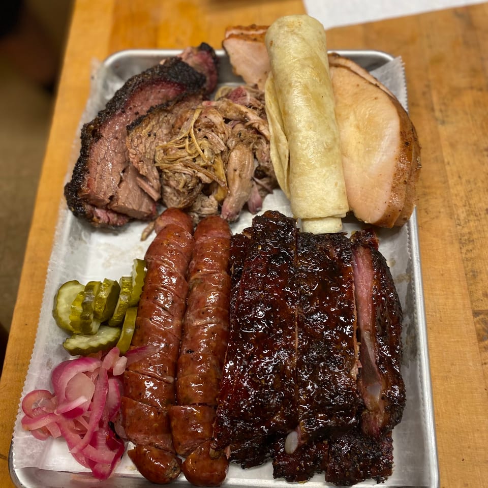 A metal tray filled with various smoked meats, pickles, pickled onions, and a tortilla.