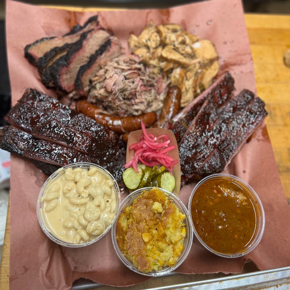 A large platter of barbecue meats including brisket, ribs, pulled pork, and sausage, with sides.