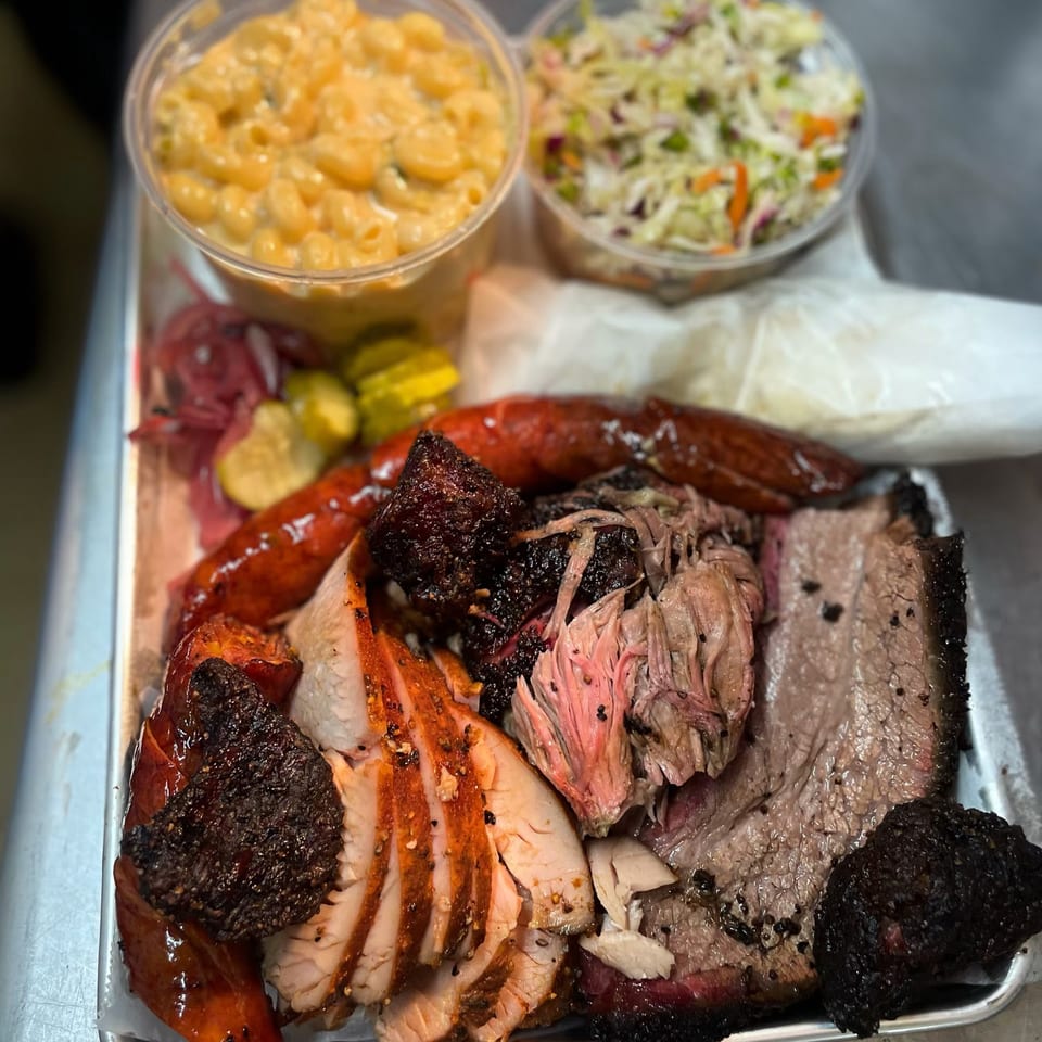 A BBQ platter with brisket, pulled pork, sliced turkey, sausage, mac and cheese, and coleslaw.