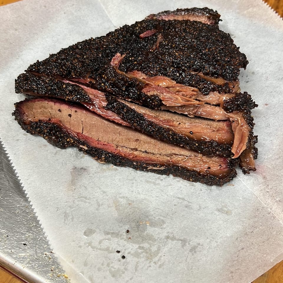 Slices of smoked brisket with a dark, peppery bark and a pink smoke ring on white butcher paper.