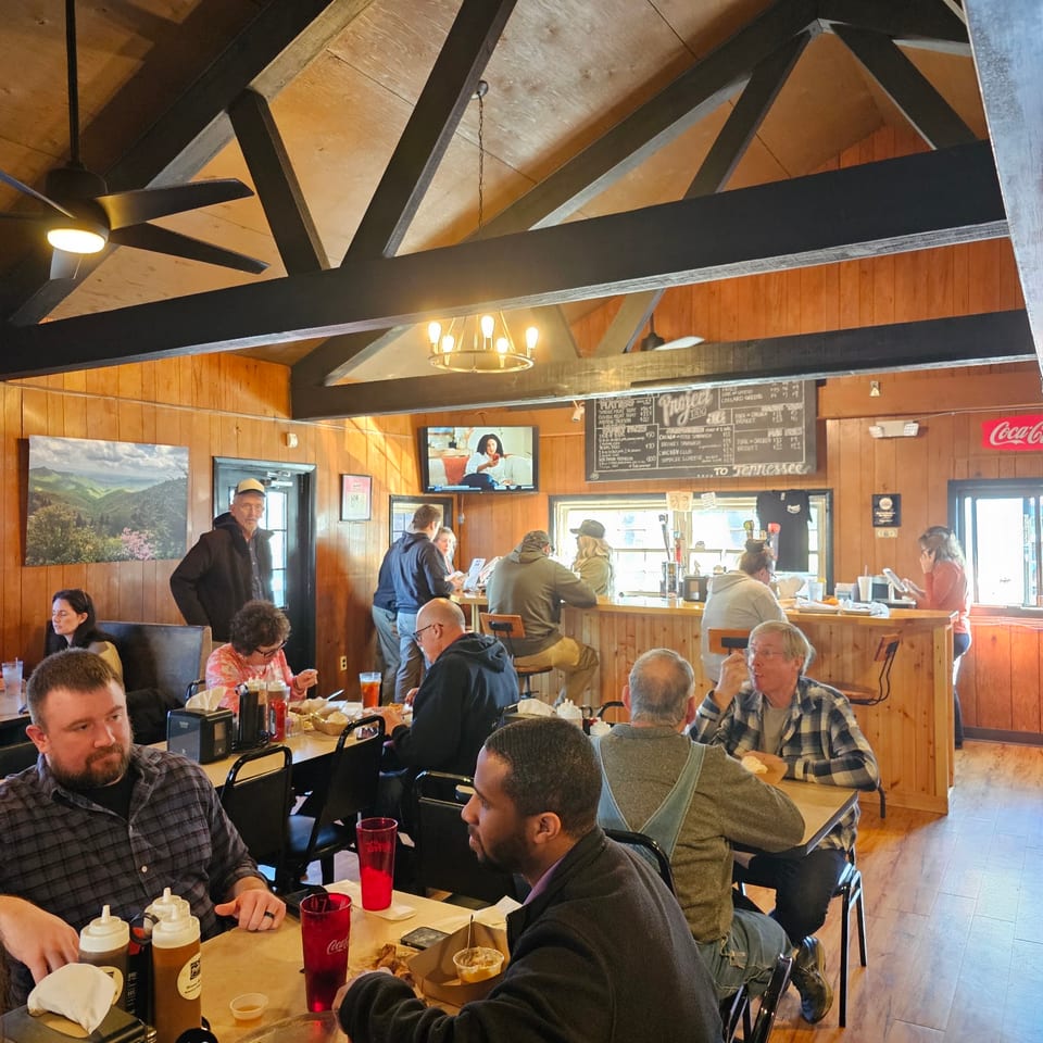 Diners enjoying meals and drinks at tables and a bar in a rustic restaurant with wood paneling.