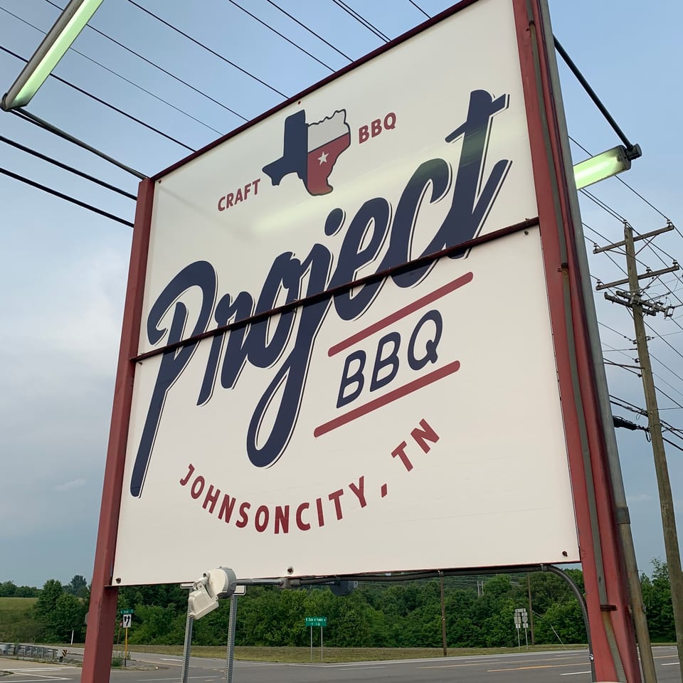 A large white sign for Project BBQ in Johnson City, TN, with a Texas-shaped logo.
