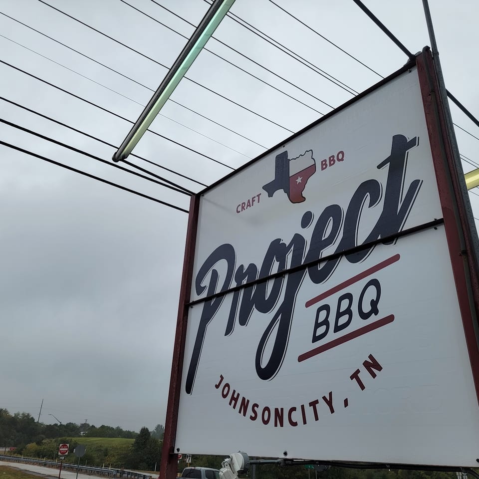 Project BBQ sign in Johnson City, TN, with a Texas map logo, against a cloudy sky.